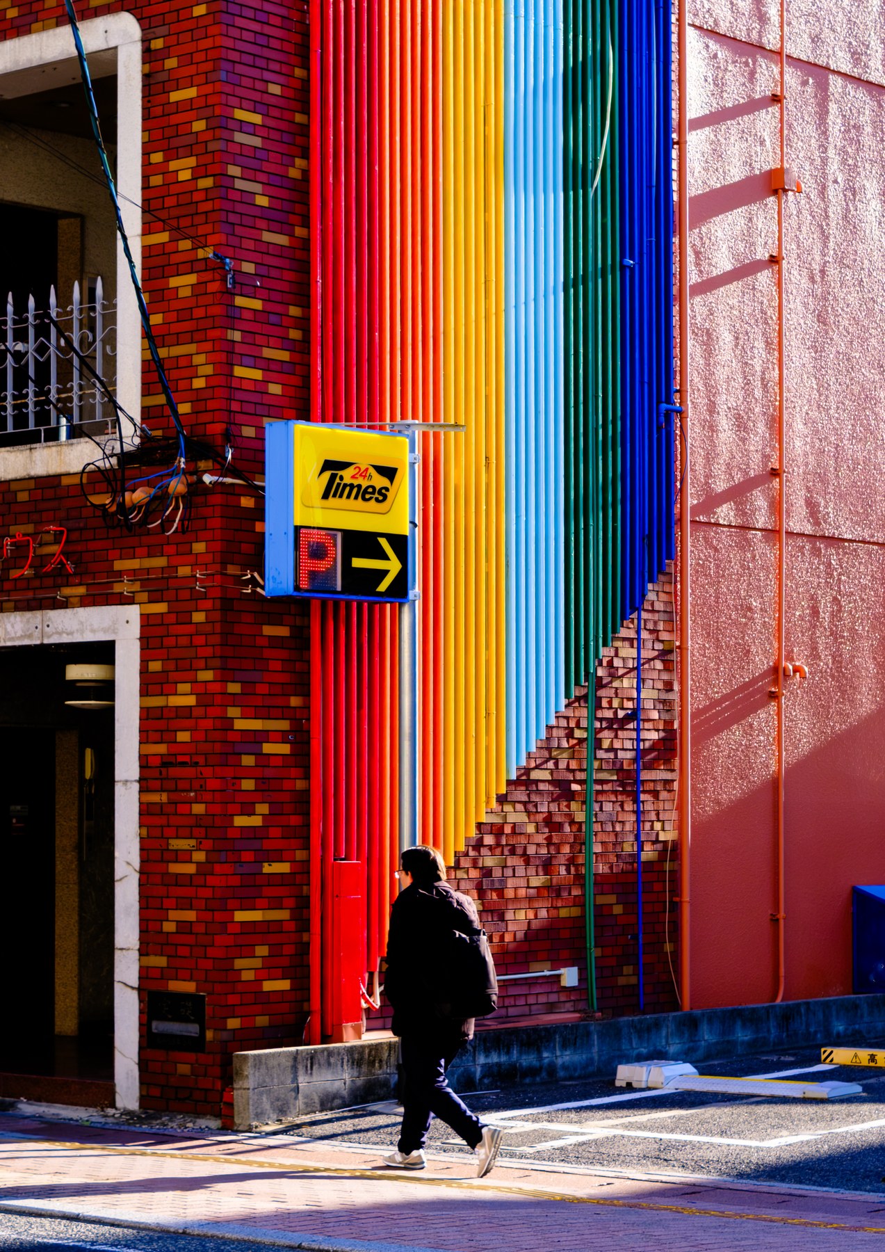 A person walking past a building facade made of brightly coloured vertical panels.